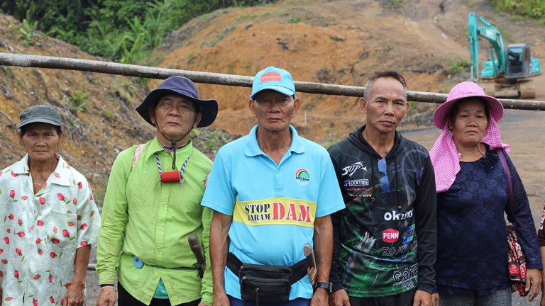 Five indigenous Penan villagers stand before a logging blockade.